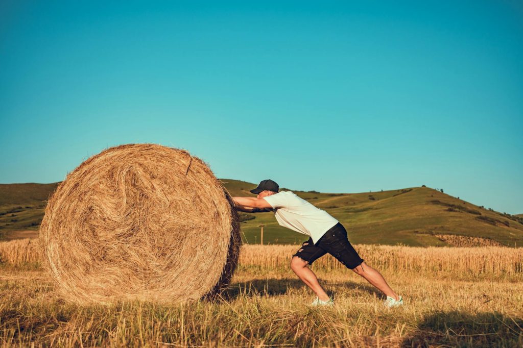 man pushing a hay bale by himself